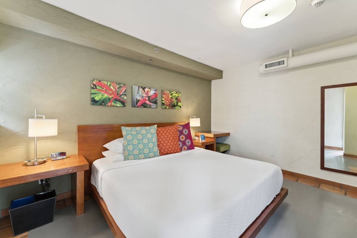 A hotel room with a bed, two bedside tables, a nightstand, a mirror, and artwork on the wall.