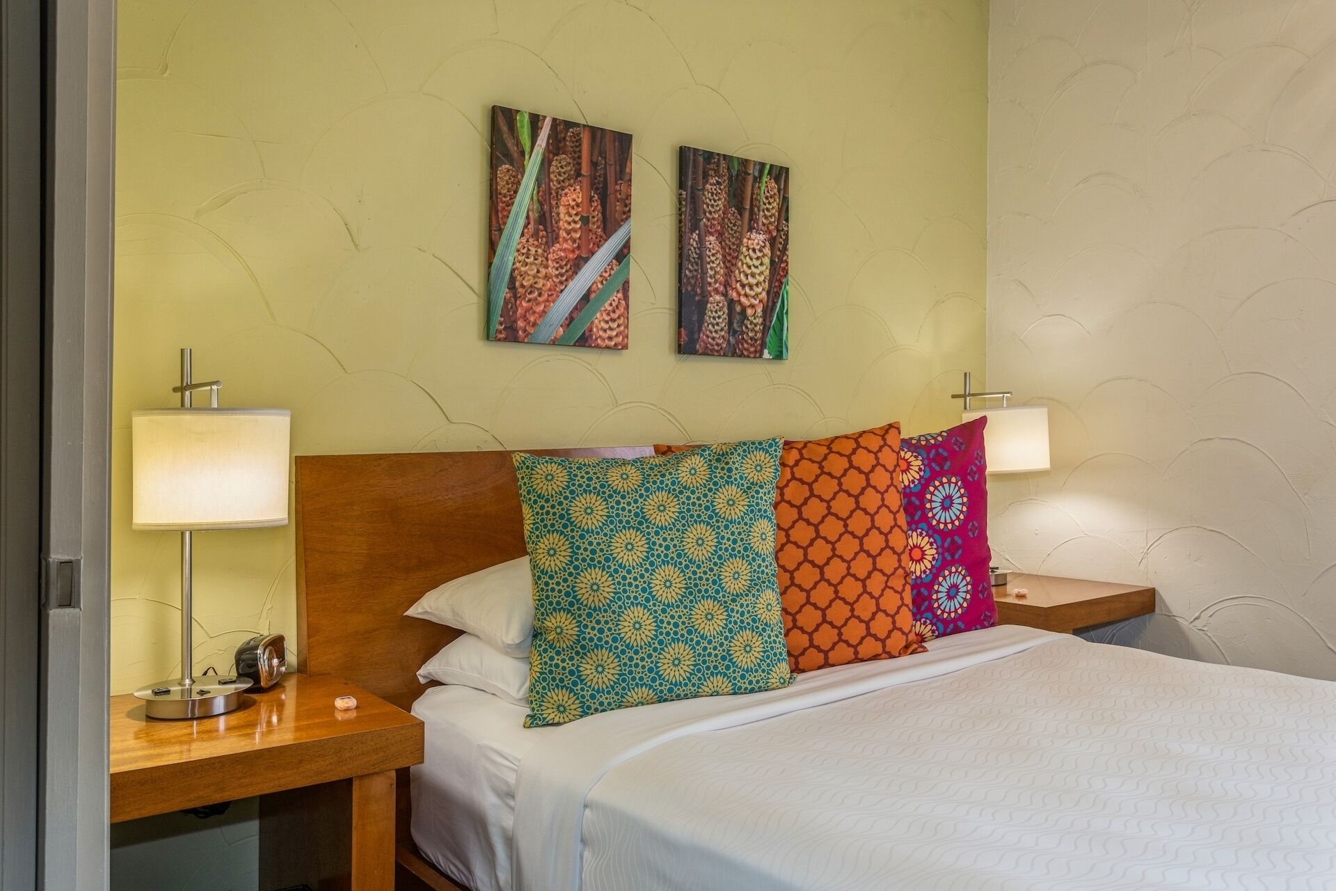 A neatly made bed with patterned pillows, a wooden headboard, and two wall-mounted lamps.