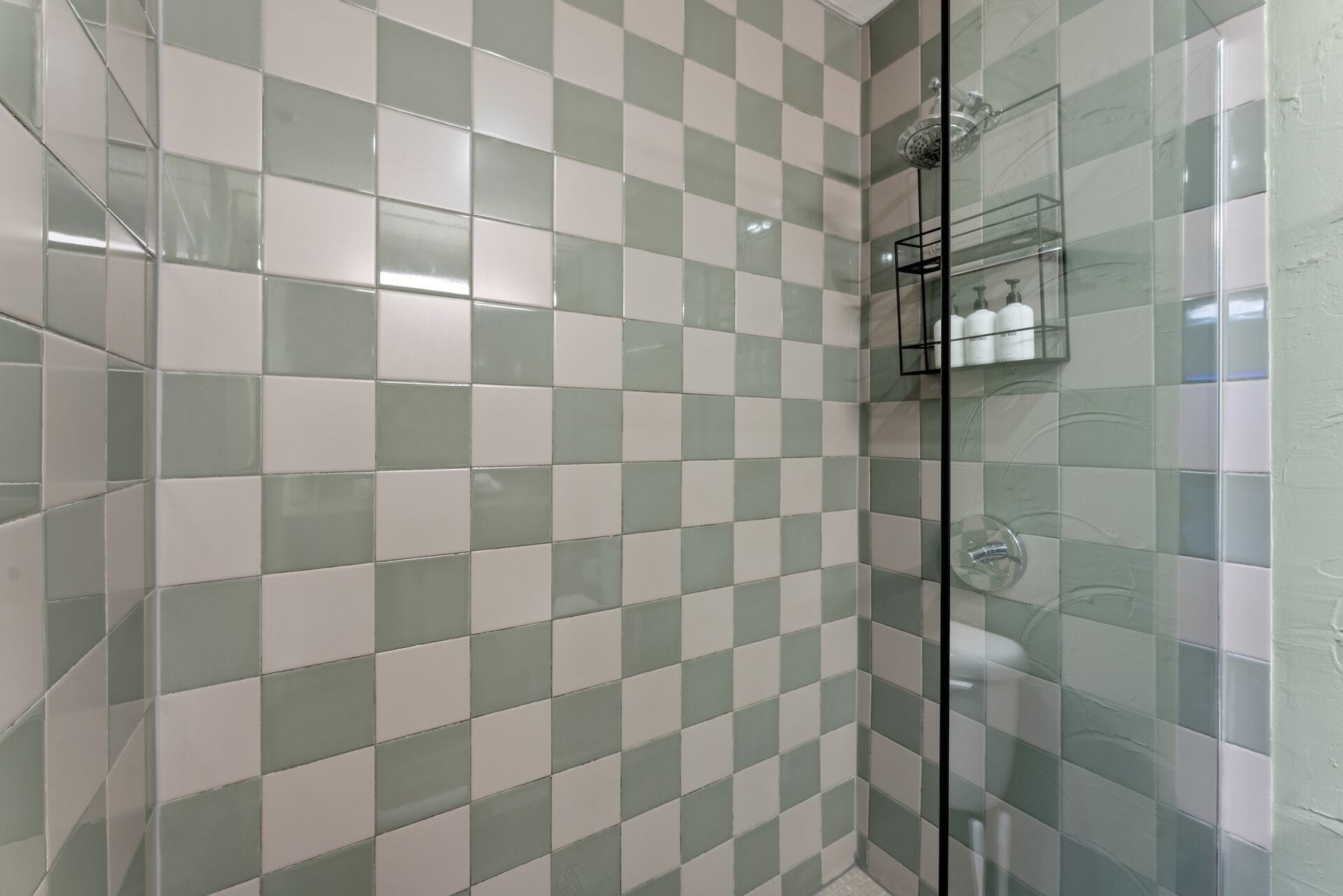 A shower area with checkered tile walls, a glass shower enclosure, and a glass shelf with toiletries.