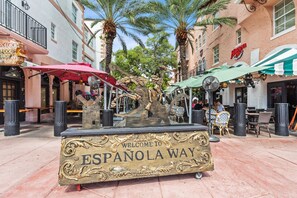 Un letrero decorativo da la bienvenida a ESPANOLA WAY, rodeado de mesas al aire libre y palmeras.