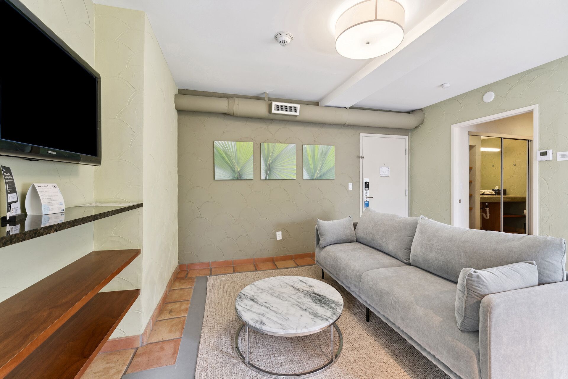 A modern living room with a grey sofa, a marble coffee table, and a flat-screen TV mounted on the wall.
