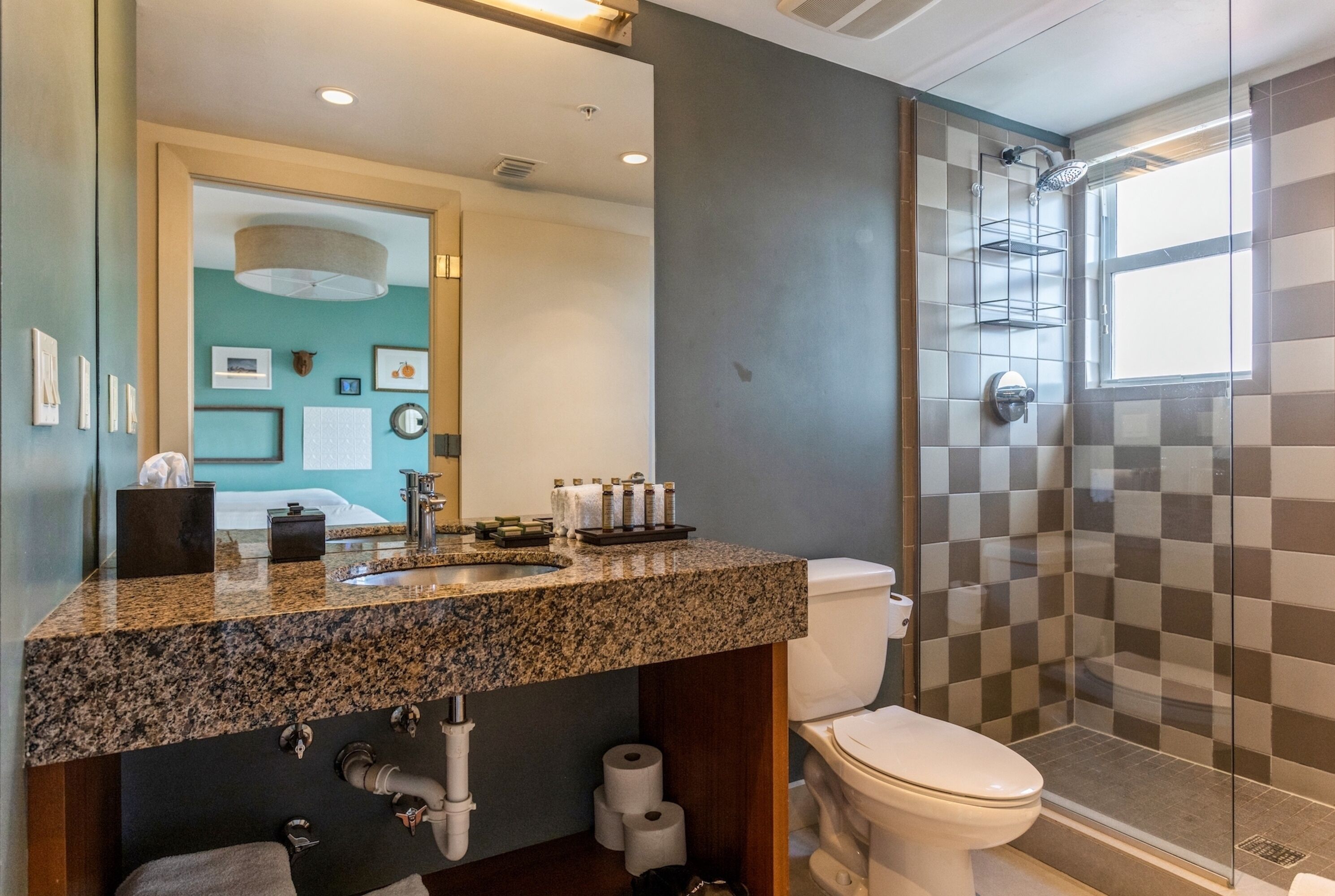 A modern bathroom with a granite countertop, a toilet, a shower with a glass door, and a visible window.