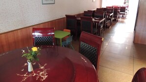 A dining area with multiple tables and chairs, a painting on the wall, and a vase with flowers on one table. - AM Flughafen (KOLN)