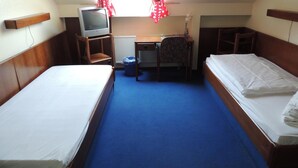 A room with two beds, a desk with a computer, and a window with red curtains. - AM Flughafen (KOLN)