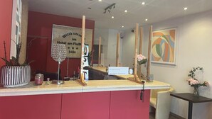 A reception desk with a red wall, a welcome sign, a potted plant, and a framed abstract painting. - AM Flughafen (KOLN)