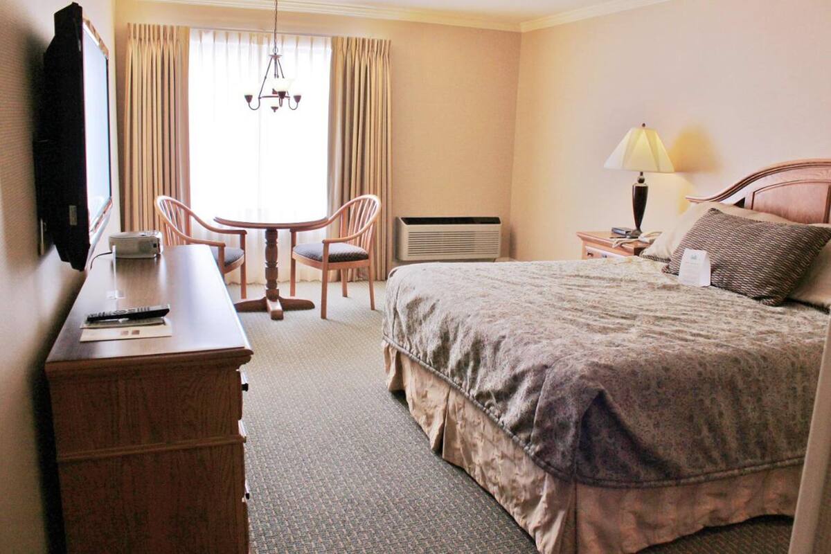 A hotel room with a bed, a desk with a chair, a television, and a window with curtains.