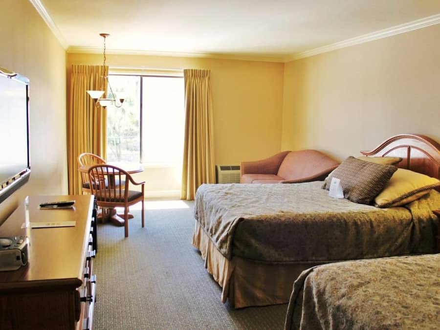 Une chambre d’hôtel avec deux lits, un bureau avec une télévision, une chaise et une fenêtre avec des rideaux.