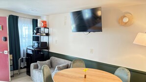 Un espacio habitable compacto con kitchenette, un televisor de pantalla plana montado en la pared, una mesa de comedor redonda de madera con cuatro sillas y un sofá.