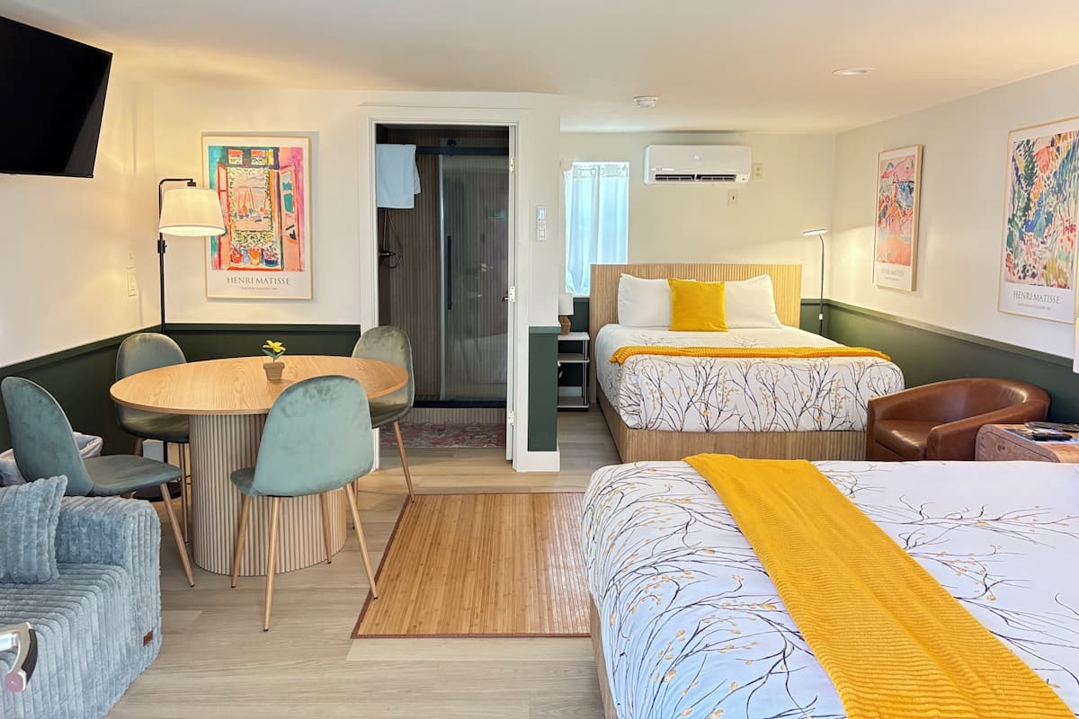A hotel room with a bed, a desk, a chair, a sofa, and a dining table.