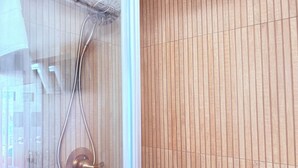 Ducha con manguera curva y grifo metálico, toallero y pared de azulejos con líneas verticales.