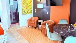 Una habitación moderna con sofá, sillas, una mesa de comedor, televisión y un cuadro abstracto colorido.