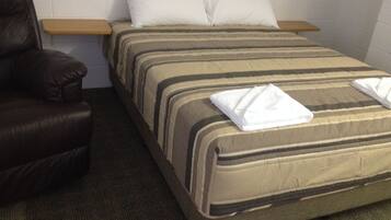 Una cama individual con una colcha a rayas, dos almohadas, una toalla blanca doblada y un sillón de cuero.