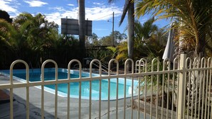 A swimming pool with a white metal fence, surrounded by palm trees and greenery. - Bororen Motel (Bororen)