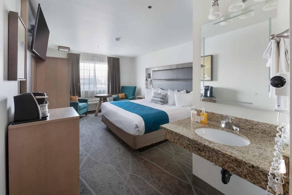 A hotel room with a bed, a desk, a chair, a TV, a bathroom with a sink and mirror, and a window with curtains.