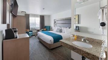 A hotel room with a bed, a desk, a chair, a TV, a bathroom with a sink and mirror, and a window with curtains.