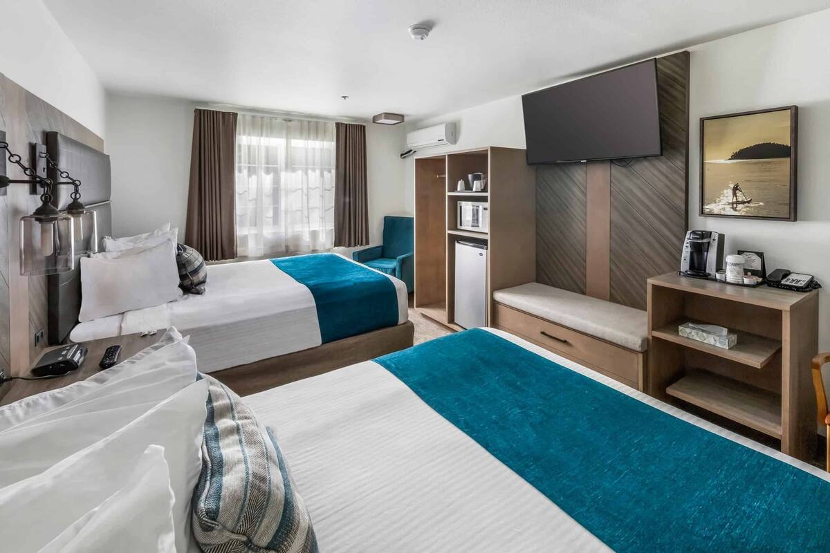 A hotel room with two beds, a TV, a desk with a coffee maker, a mini fridge, and a view of the sea.