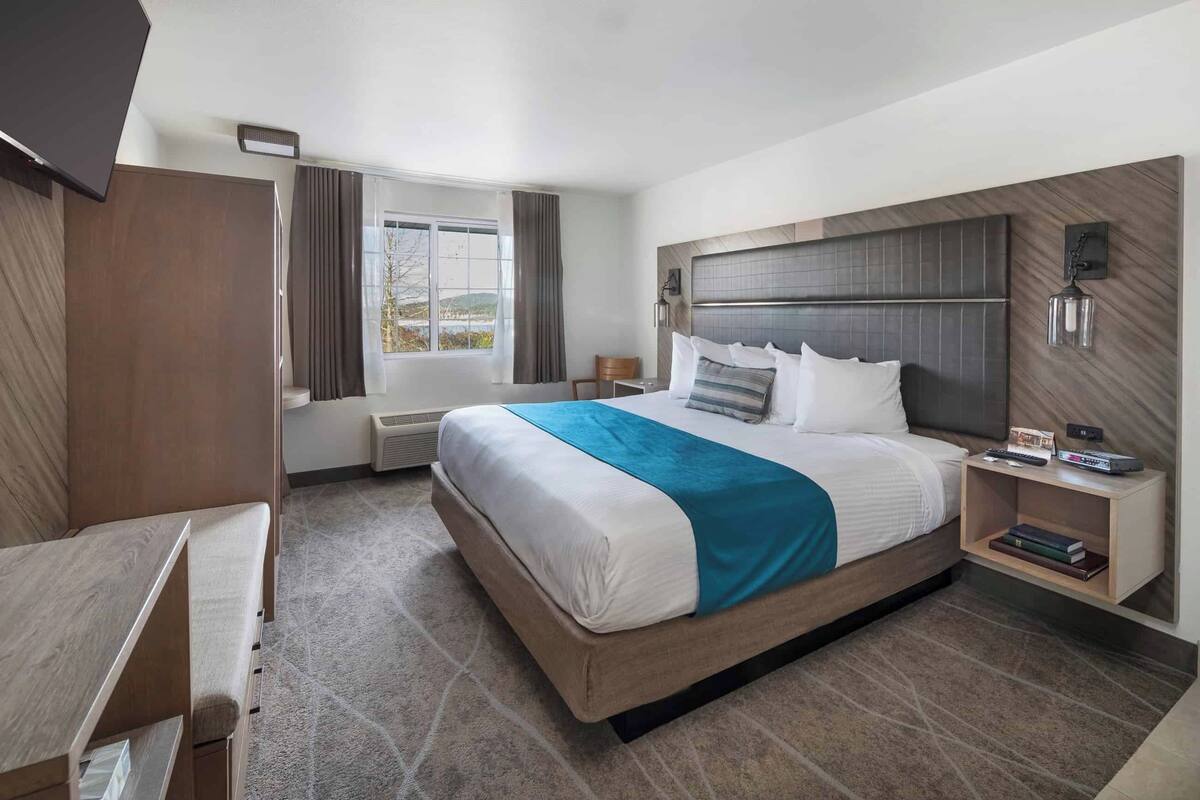 A modern hotel room with a large bed, a desk, a chair, and a small table.