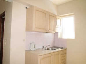 A small kitchen with wooden cabinets, a sink, and a window. - Irini Stalis (Hersonissos)