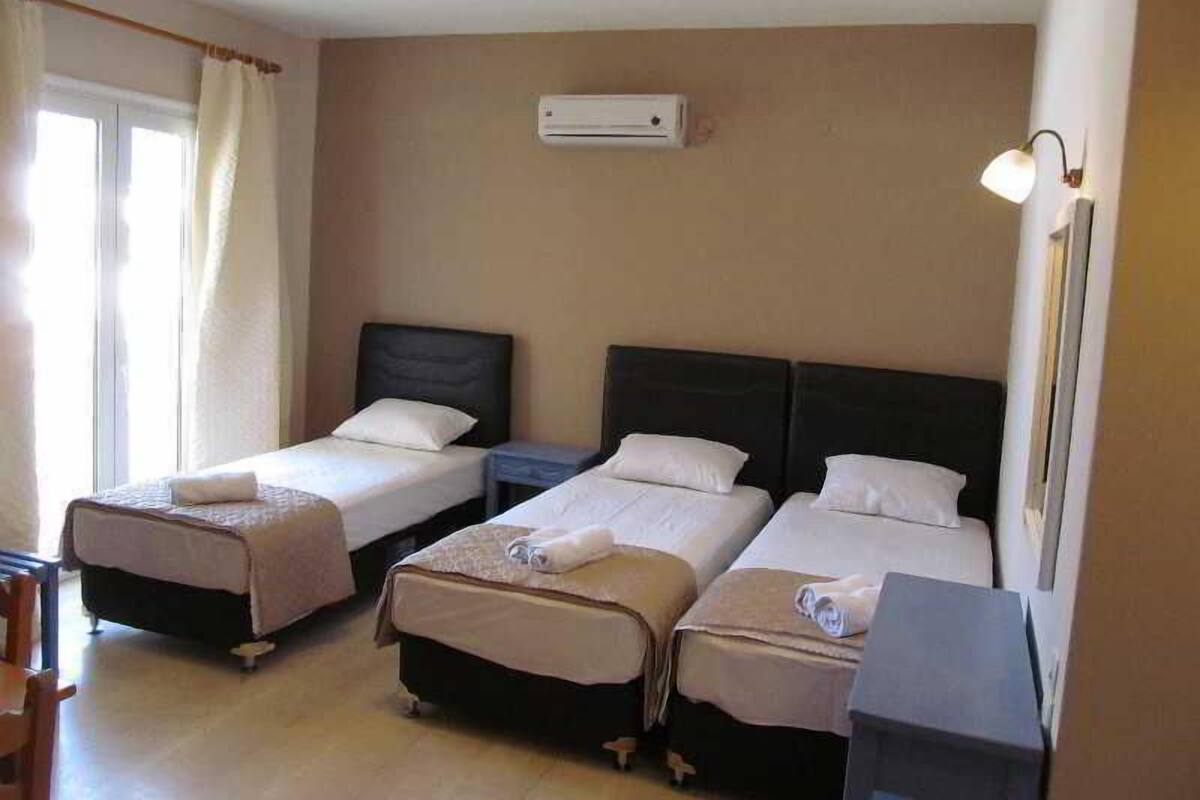 A hotel room with two single beds, a small table, a chair, and a desk.