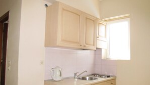 A small kitchen with wooden cabinets, a sink, and a window. - Irini Stalis (Hersonissos)