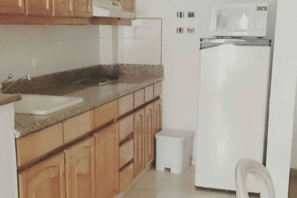 Una cocina con armarios de madera, una encimera blanca, un lavamanos, un microondas y un refrigerador.