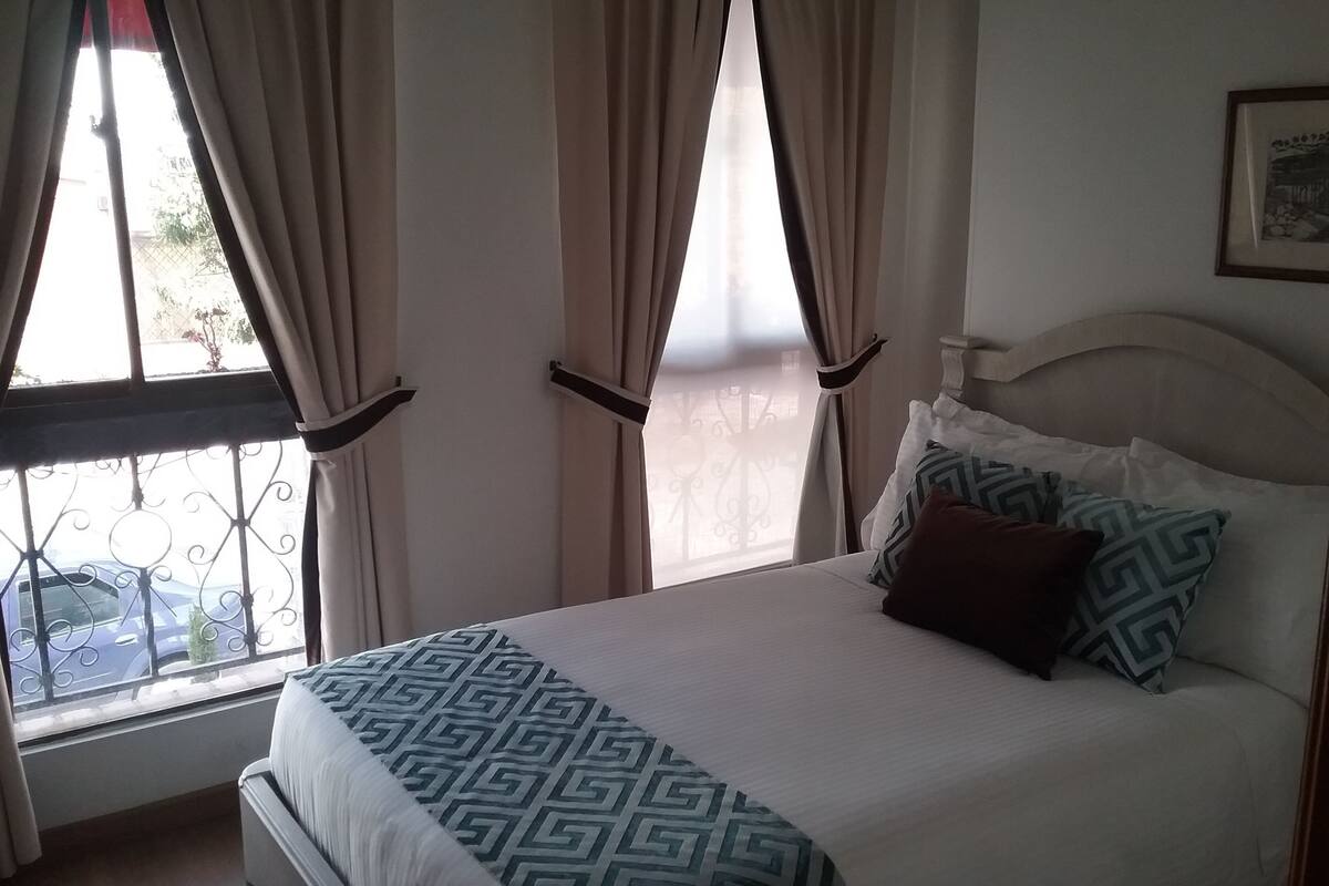 Una cama con ropa de cama estampada, cortinas y una ventana con vistas a la calle.
