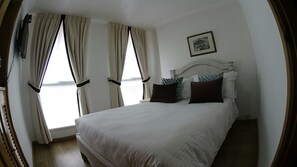 Una camera da letto con un letto grande, due finestre con tende, una testiera e un quadro incorniciato appeso al muro.