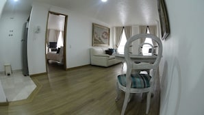 Un salon spacieux doté d’un plancher en bois, d’un canapé blanc, d’une table à manger avec des chaises et d’un tableau accroché au mur.