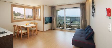 A room with a dining table, chairs, a sofa, a TV, and a balcony with a view.