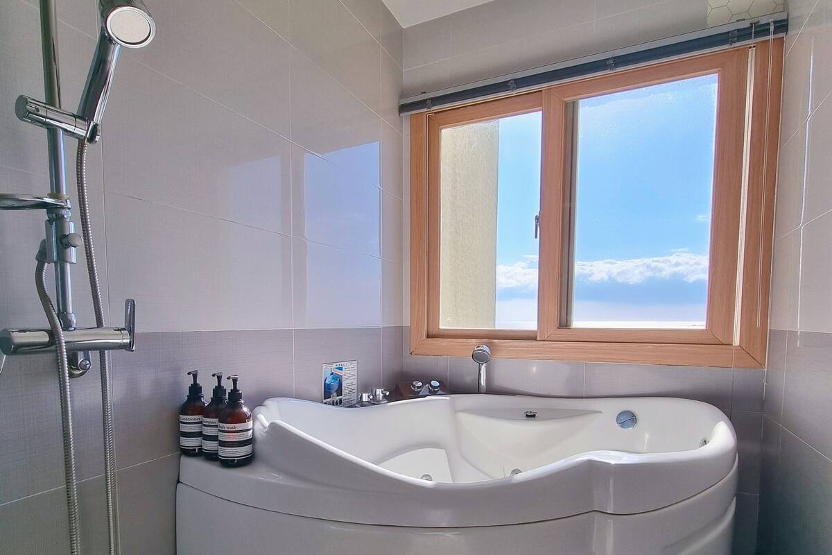 Une salle de bain moderne avec une grande baignoire sur pieds, une douche et une fenêtre offrant une vue sur le ciel.