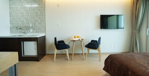 A hotel room with a bed, a small kitchenette, a TV mounted on the wall, and a table with two chairs.