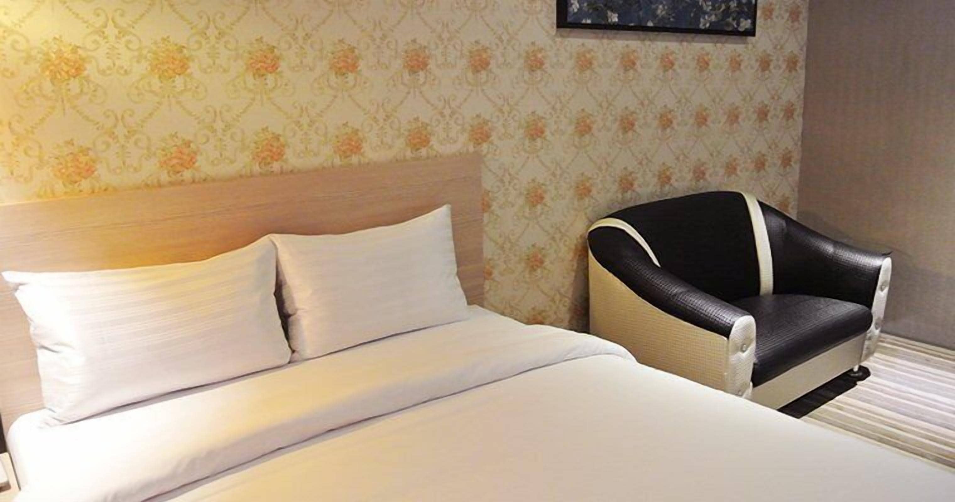A hotel room with a bed, a headboard, and a chair.