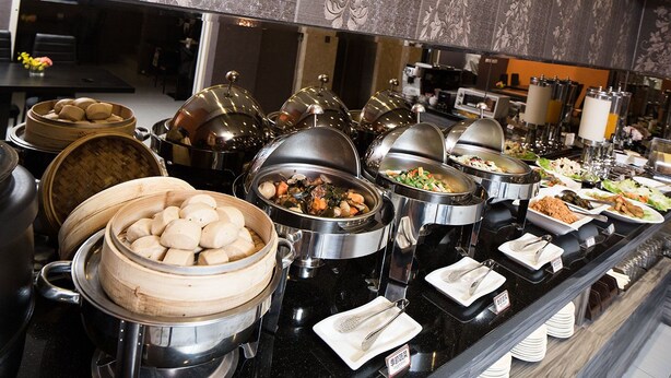Un bufé con diferentes estaciones de comida, que incluyen dumplings, verduras y otros platos.