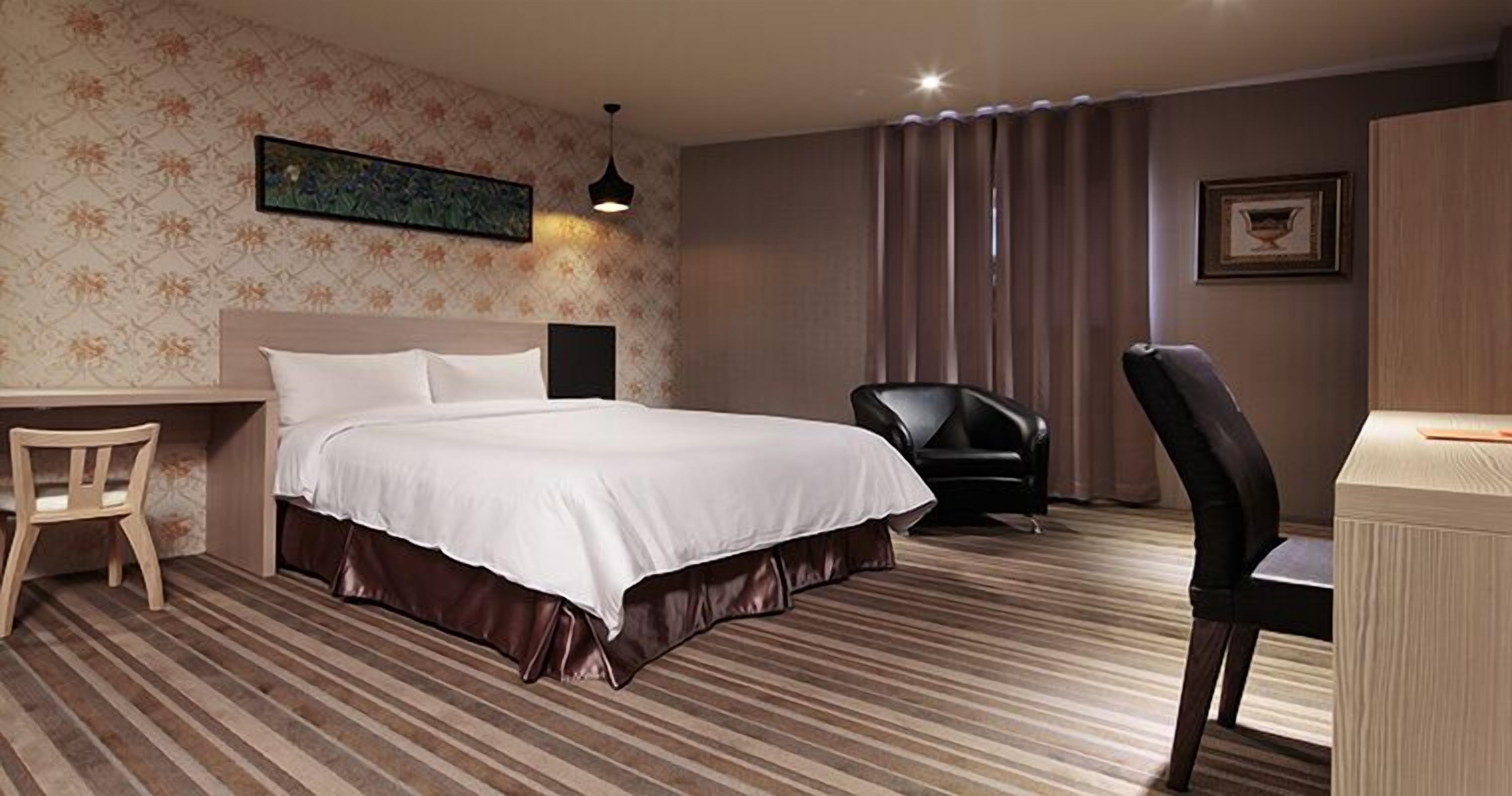 A hotel room with a large bed, a desk, a chair, and a small table.
