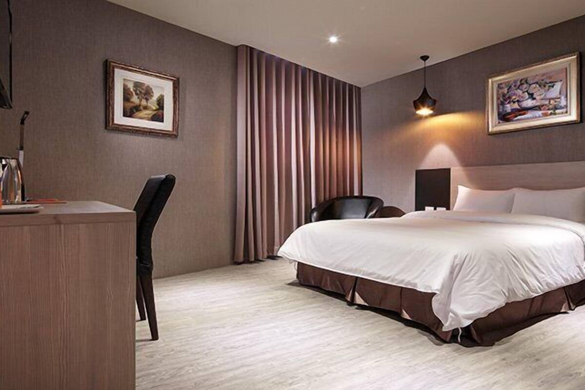 Une chambre d’hôtel avec un lit, un bureau, une chaise, une télévision et deux tableaux accrochés aux murs.