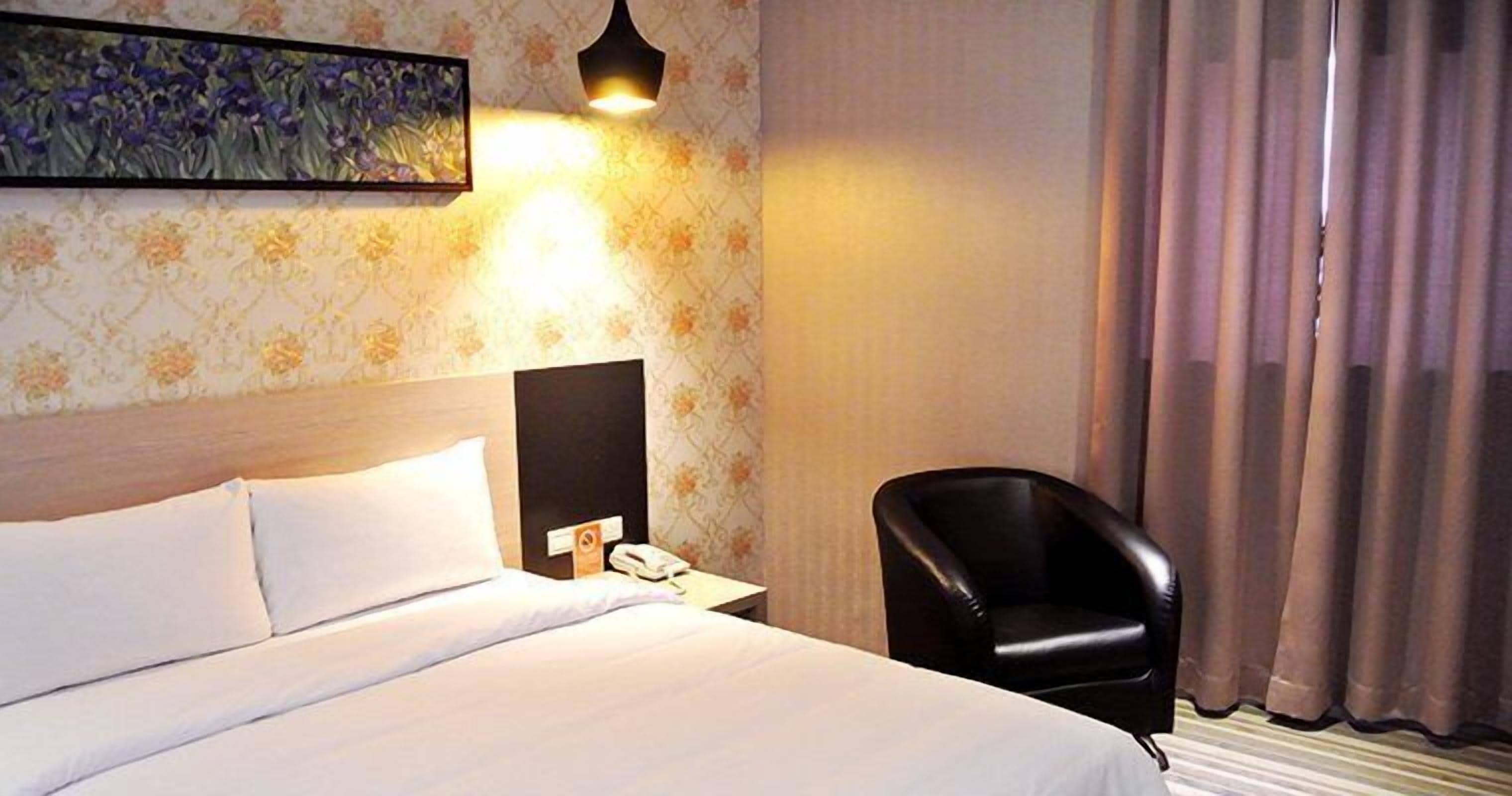 Ein Hotelzimmer mit einem Bett, einem Sessel, einem Nachttisch mit Telefon und einem Bild an der Wand.