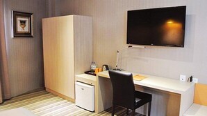 Habitación de hotel con cama, escritorio, silla, televisor, armario y refrigerador pequeño.