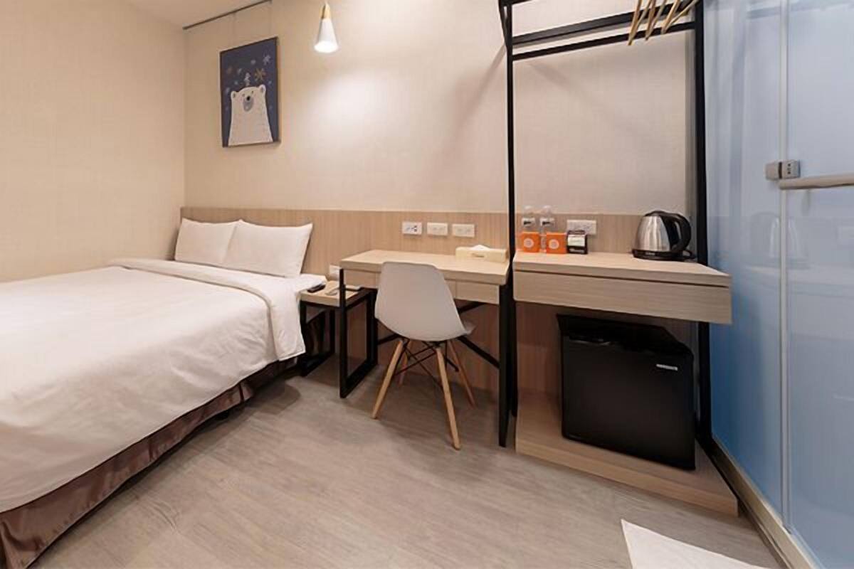 Une chambre d’hôtel équipée d’un lit, d’un bureau, d’une chaise, d’une bouilloire et d’un petit placard.