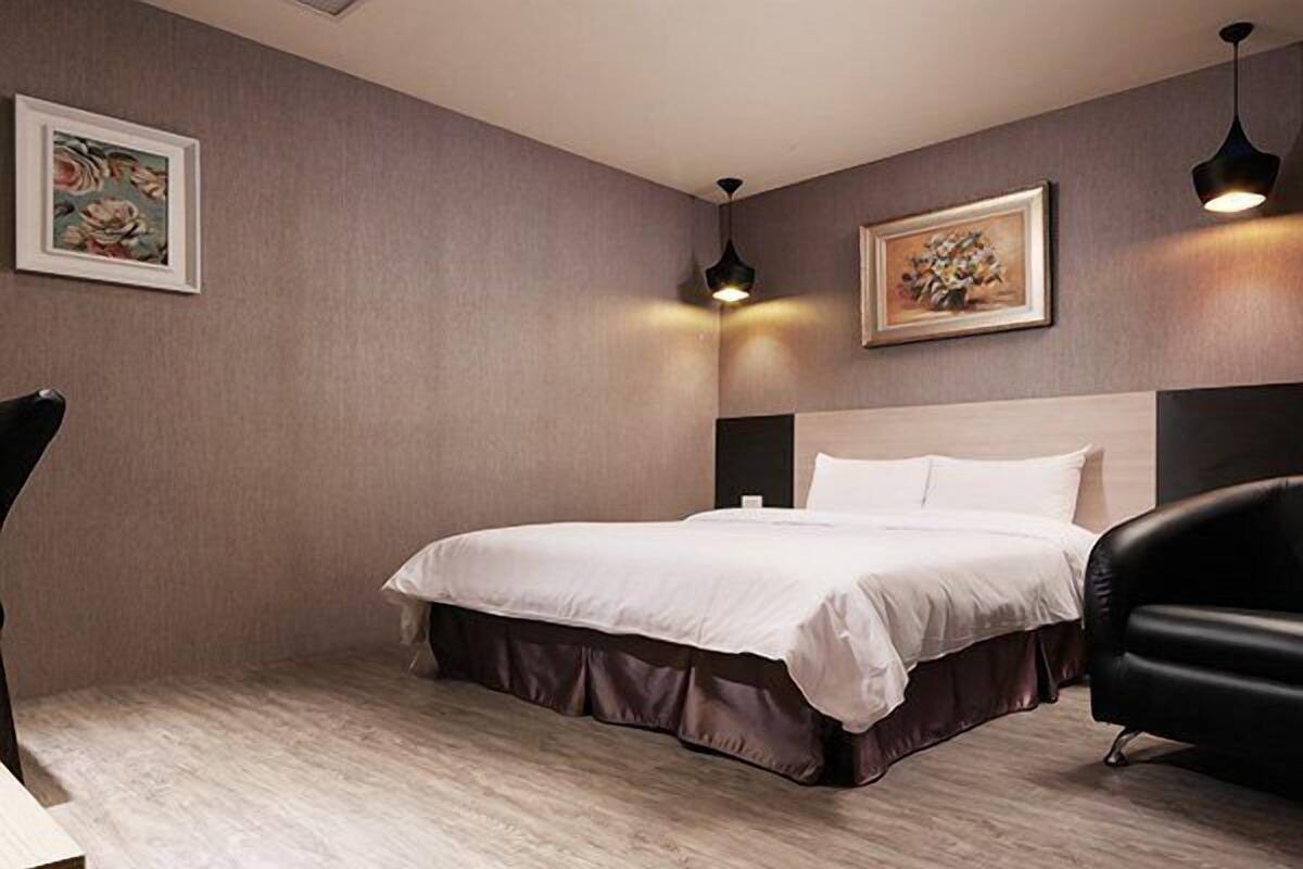 Une chambre d’hôtel avec un grand lit, un fauteuil en cuir noir et deux lampes suspendues.