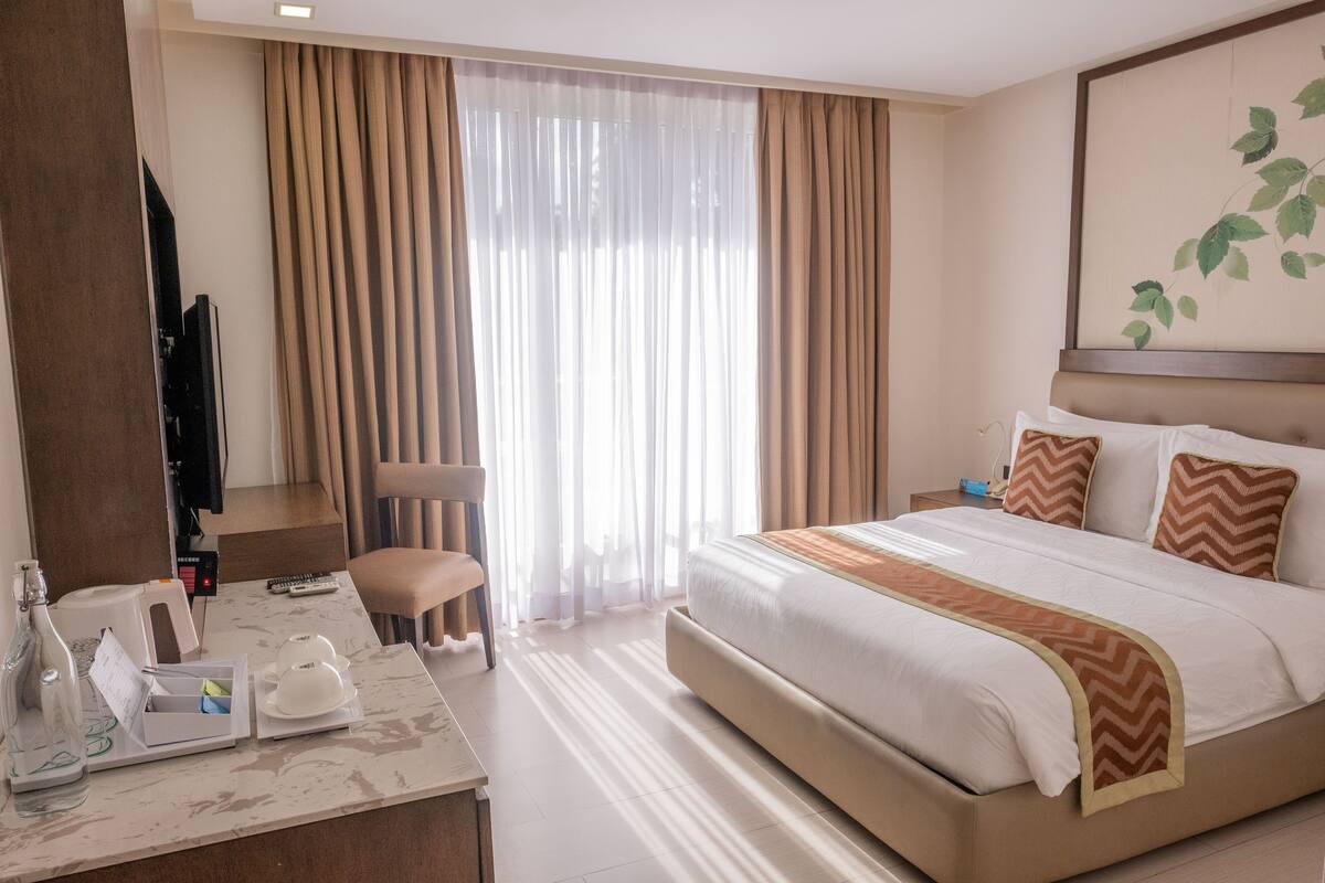 A hotel room with a large bed, a desk with a chair, a television, and a window with curtains.
