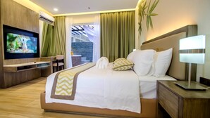 Une chambre d’hôtel moderne dotée d’un grand lit, d’un téléviseur à écran plat, d’un bureau avec une chaise, et offrant une vue sur un mur en pierre et la verdure environnante.