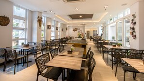 Un restaurant spacieux avec de hauts plafonds, de grandes fenêtres et un îlot central. Les tables et les chaises sont disposées autour de l’îlot, offrant ainsi différents types de sièges.