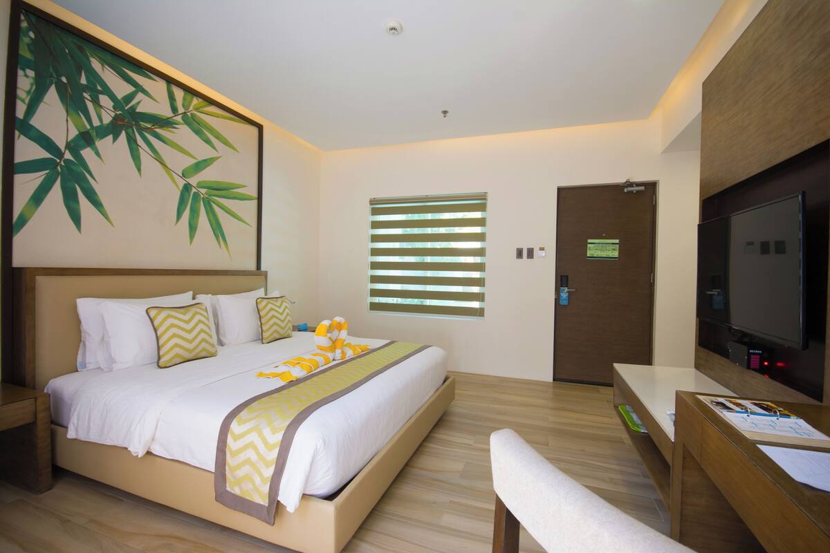 A modern hotel room with a large bed, a desk with a chair, a television, and a window with blinds.