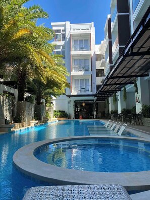 Une piscine de forme circulaire, entourée d’un bâtiment doté de balcons et d’un espace de détente extérieur.