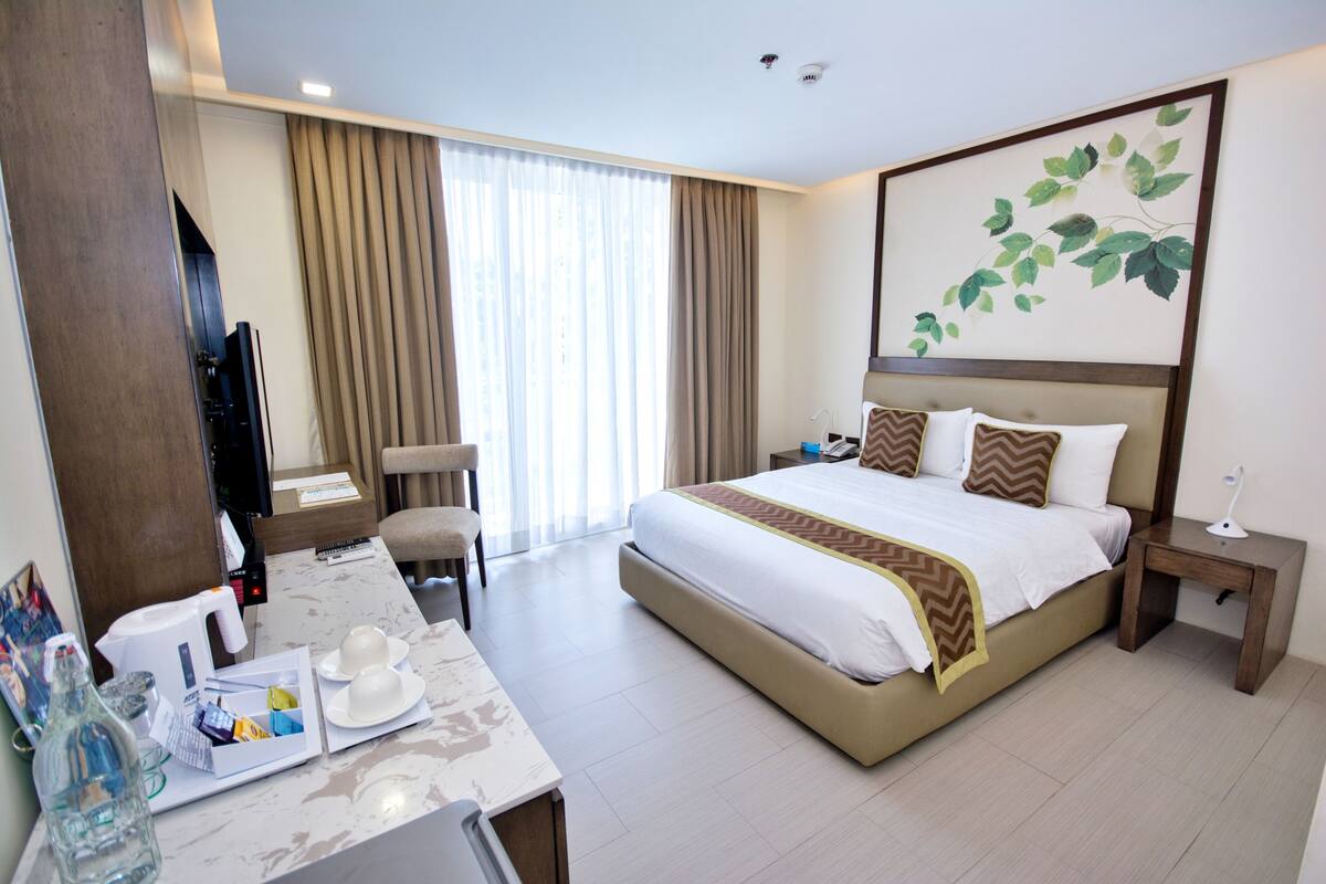 A hotel room with a large bed, a desk with a chair, a TV, and a window with curtains.