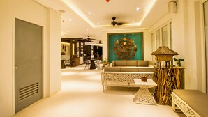 Un hall d’hôtel spacieux avec un espace salon central, un mur décoratif et un ventilateur de plafond.