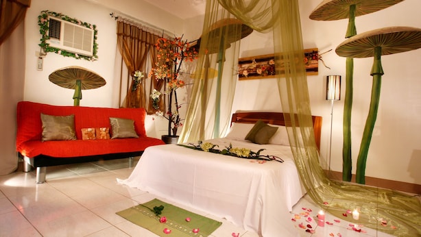 A hotel room with a red sofa, a bed with sheer curtains, and decorative umbrellas.