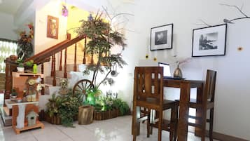 A dining area with wooden chairs and a table, surrounded by potted plants and a staircase.