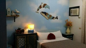 A bedroom with a bed, a nightstand with a lamp, decorative wall art, and a small shelf with a teddy bear and a bird.