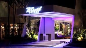 Een moderne hotelentree met een neonbord, een overdekt terras en een zwembad.